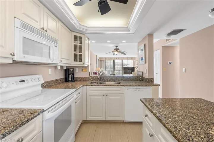 Kitchen featuring white appliances, sink, white cabinetry, ceiling fan, and dark stone counters