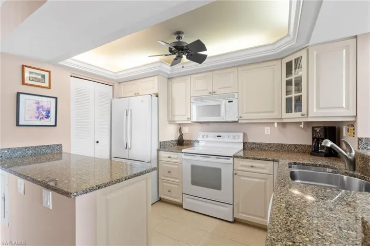 Kitchen with sink, dark stone countertops, white appliances, and a raised ceiling