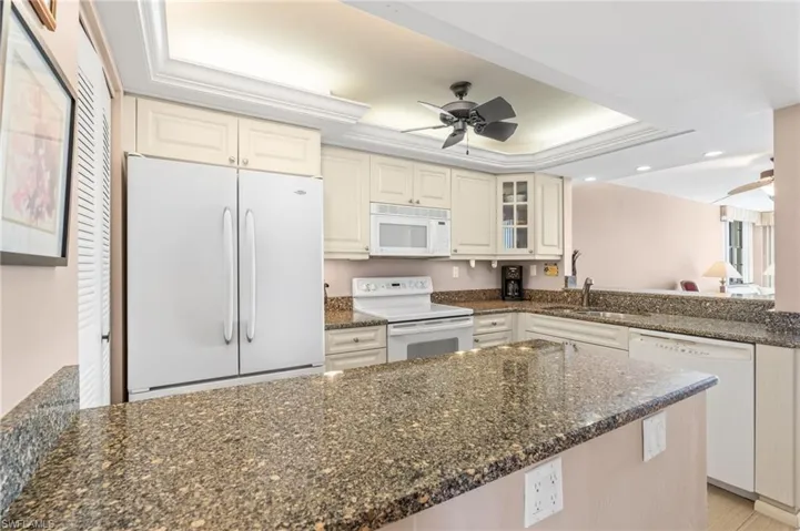 Kitchen featuring white appliances, a tray ceiling, white cabinetry, ceiling fan, and dark stone counters
