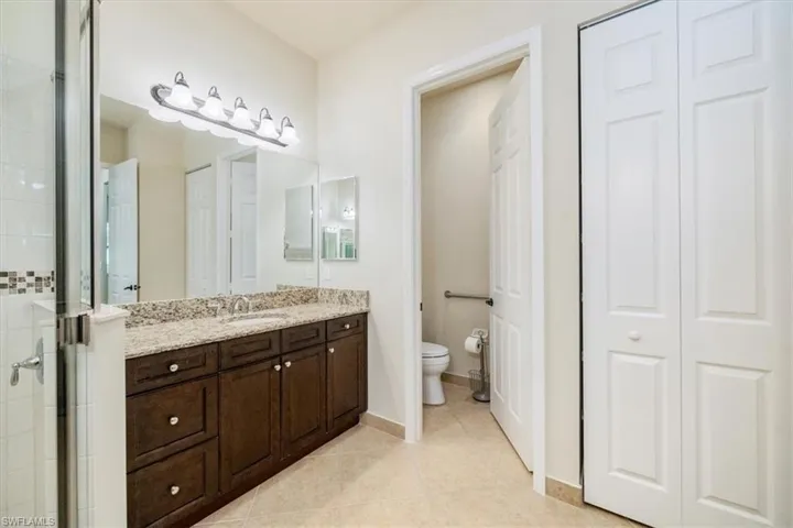 Full bath featuring tile patterned flooring, vanity, tiled shower, toilet, and a closet