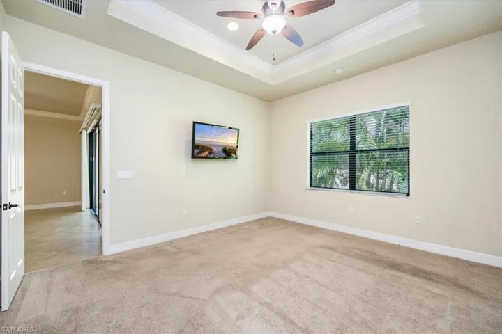 Empty room with a ceiling fan, ornamental molding, a tray ceiling, and light carpet