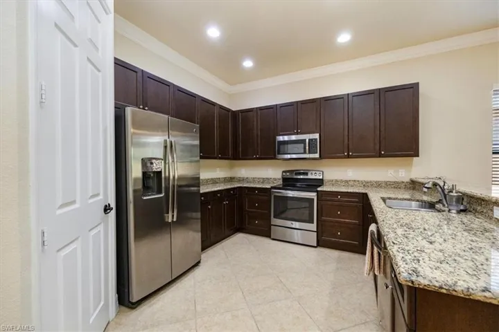 Kitchen featuring stainless steel appliances, crown molding, and light stone counters