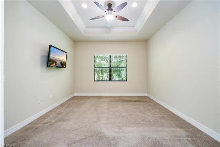 Carpeted empty room featuring a tray ceiling, crown molding, baseboards, ceiling fan, and recessed lighting
