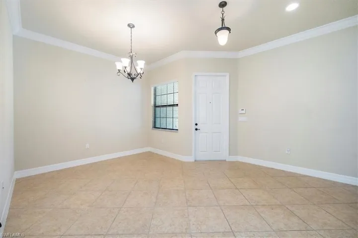 Spare room featuring light tile patterned flooring, ornamental molding, baseboards, and a chandelier