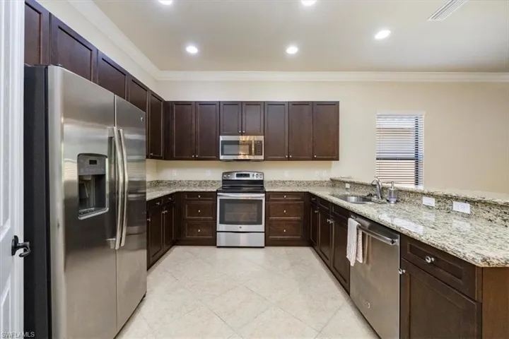 Kitchen featuring crown molding, dark brown cabinetry, a sink, a peninsula, and stainless steel appliances