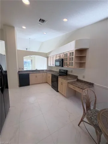 Kitchen featuring glass fronted cabinets, black appliances, light marble finish floors, open shelves, and vaulted ceiling