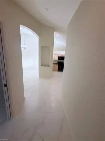 Corridor featuring light marble finish floors, arched walkways, hanging lights, and a textured wall