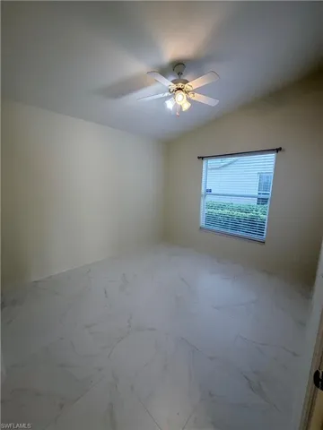 Spare room with vaulted ceiling, marble finish flooring, and a ceiling fan