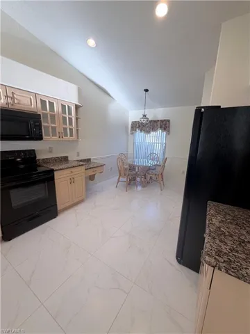 Kitchen with black appliances, hanging light fixtures, vaulted ceiling, light marble finish floors, and glass fronted cabinets