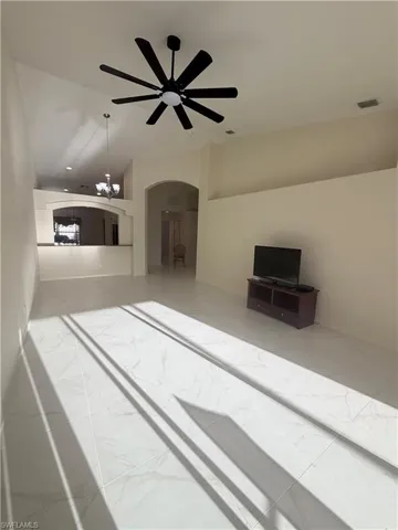 Unfurnished living room with light marble finish flooring, arched walkways, a ceiling fan, vaulted ceiling, and a chandelier