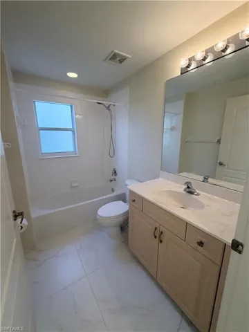 Bathroom with vanity, shower / washtub combination, and light marble finish flooring