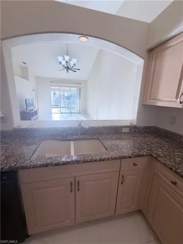 Kitchen with black dishwasher, dark stone counters, and lofted ceiling