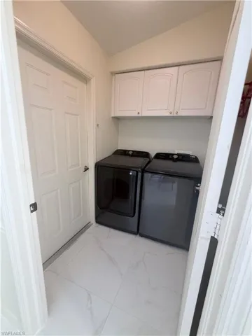 Laundry room with lofted ceiling, light marble finish floors, cabinet space, and washing machine and clothes dryer