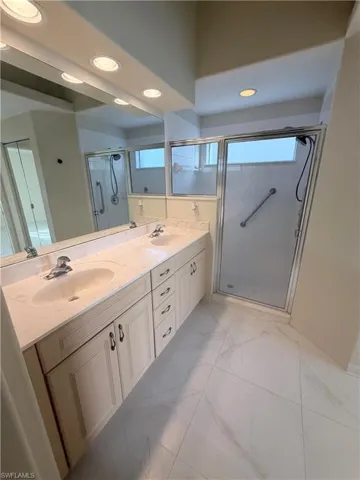 Bathroom featuring double vanity, recessed lighting, a shower stall, and light marble finish flooring