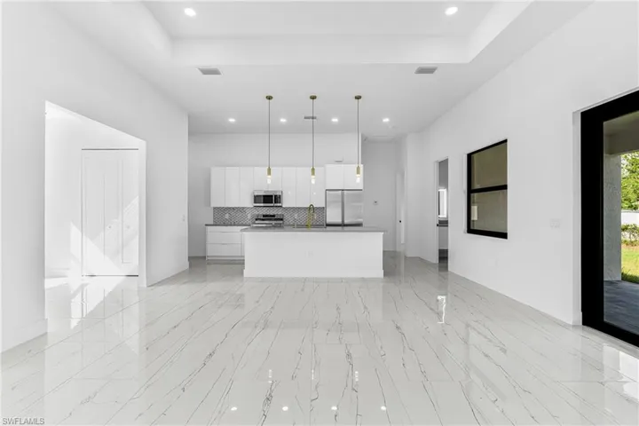 Kitchen with open floor plan, an island with sink, white cabinets, stainless steel appliances, and hanging light fixtures