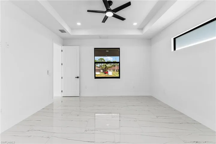 Unfurnished room featuring a tray ceiling, light marble finish flooring, a ceiling fan, and recessed lighting