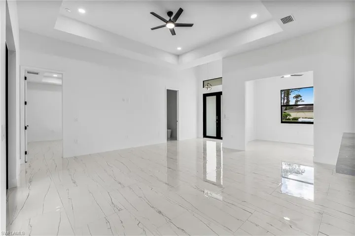 Unfurnished living room featuring a ceiling fan, a tray ceiling, recessed lighting, and light marble finish flooring