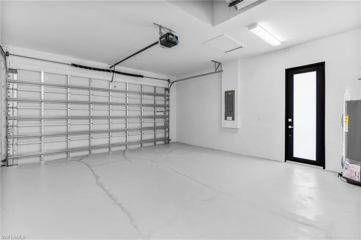 Garage with electric water heater, electric panel, and a garage door opener