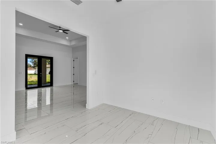 Empty room featuring a tray ceiling, recessed lighting, ceiling fan, light marble finish floors, and french doors