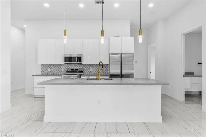 Kitchen with white cabinetry, pendant lighting, stainless steel appliances, and dark stone counters