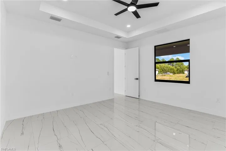 Empty room with a raised ceiling, recessed lighting, a ceiling fan, and light marble finish flooring
