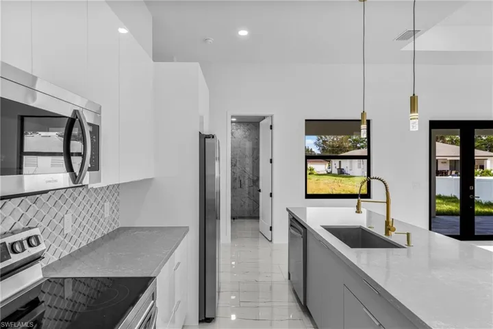 Kitchen featuring modern cabinets, stainless steel appliances, french doors, dark stone countertops, and tasteful backsplash