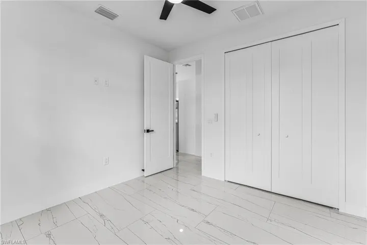 Unfurnished bedroom with ceiling fan, light marble finish flooring, and a closet