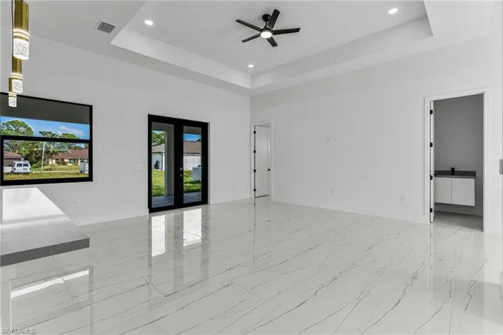Unfurnished room with french doors, ceiling fan, a tray ceiling, recessed lighting, and light marble finish flooring