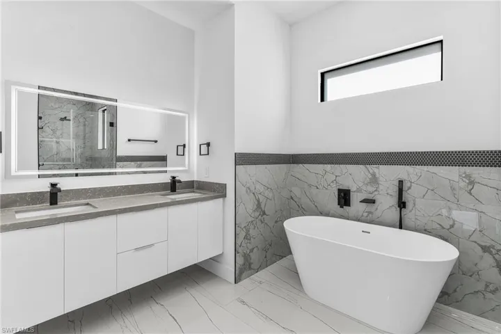 Full bathroom with double vanity, a marble finish shower, a freestanding tub, light marble finish flooring, and tile walls