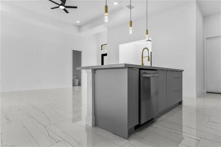 Kitchen with ceiling fan, a center island with sink, a high ceiling, modern cabinets, and light marble finish floors