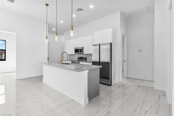 Kitchen with stainless steel appliances, a kitchen island with sink, white cabinetry, and light marble finish floors