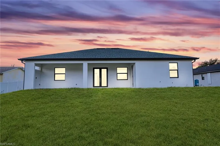 Back of property with stucco siding, a yard, and roof with shingles