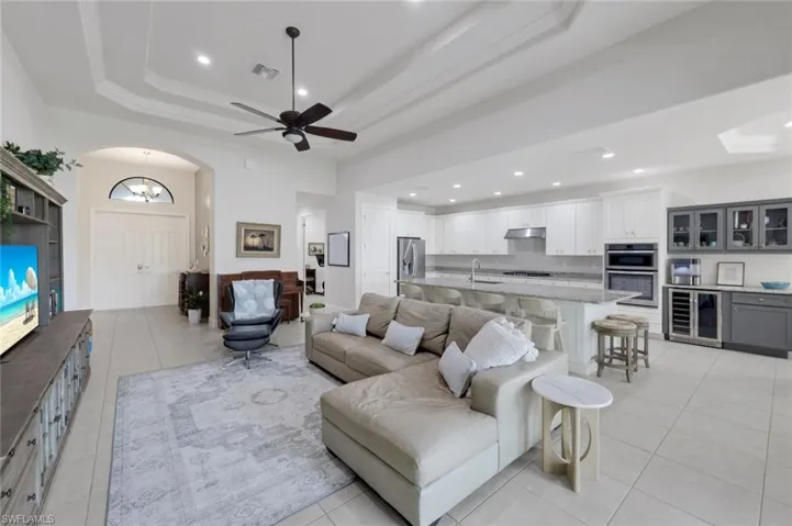 Living area with a ceiling fan, beverage cooler, arched walkways, light tile patterned floors, and a raised ceiling