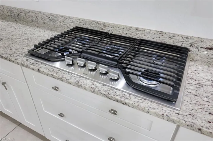 Kitchen view of stainless steel gas cooktop, light stone counters, and white cabinets
