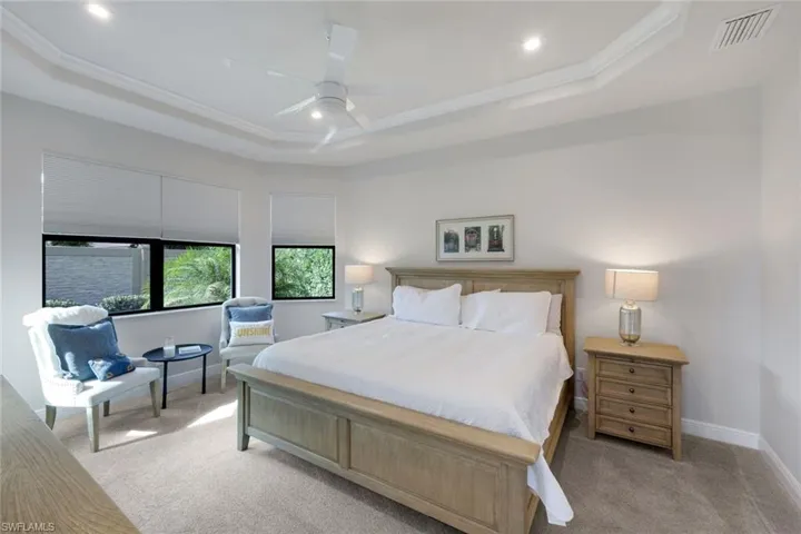 Bedroom with ornamental molding, ceiling fan, a tray ceiling, and light carpet
