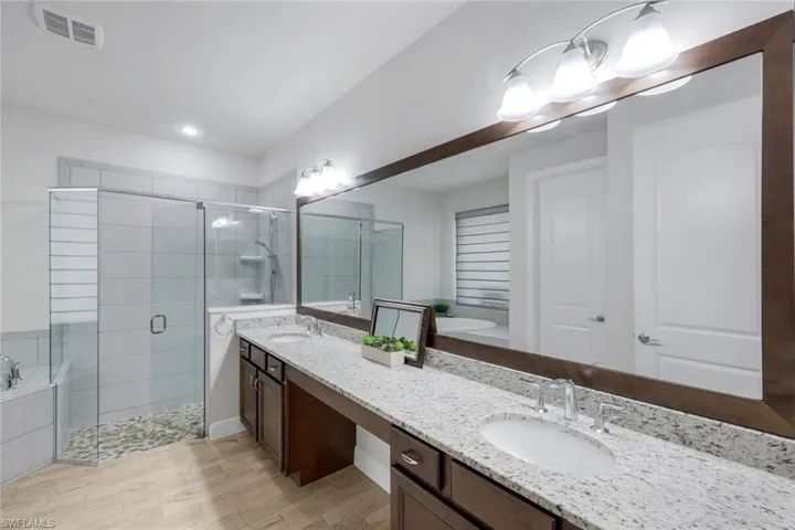 Full bathroom featuring a bath, double vanity, a stall shower, and light wood-style floors