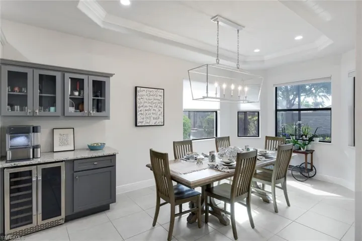 Dining space featuring beverage cooler, plenty of natural light, a raised ceiling, a chandelier, and crown molding