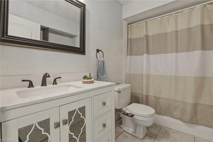 Bathroom with vanity, a textured wall, light tile patterned floors, and shower / tub combo with curtain
