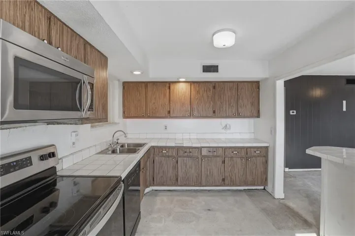Kitchen with stainless steel appliances, wood finish cabinetry, concrete flooring, tile counters, and recessed lighting