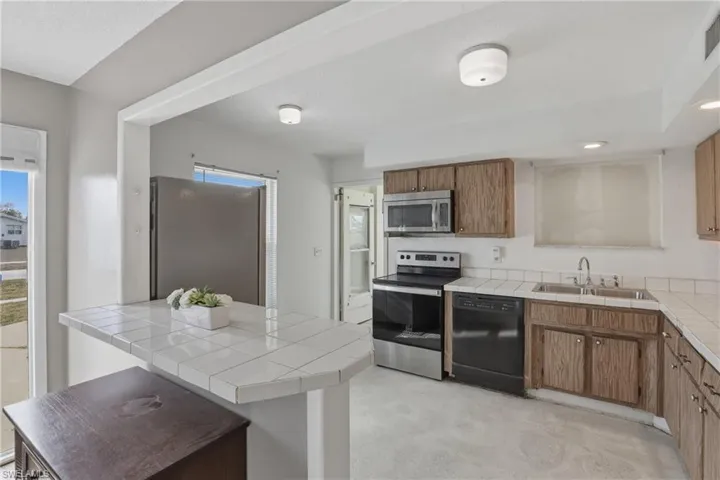 Kitchen featuring tile counters, stainless steel appliances, wood finish cabinetry, a breakfast bar, and recessed lighting
