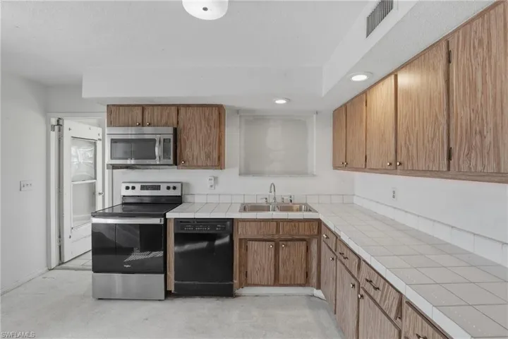Kitchen with stainless steel appliances, tile countertops, recessed lighting, and wood finish cabinets