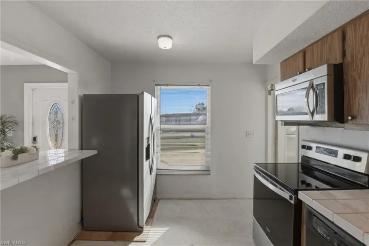 Kitchen featuring tile counters, stainless steel appliances, a textured ceiling, and wood finish cabinetry