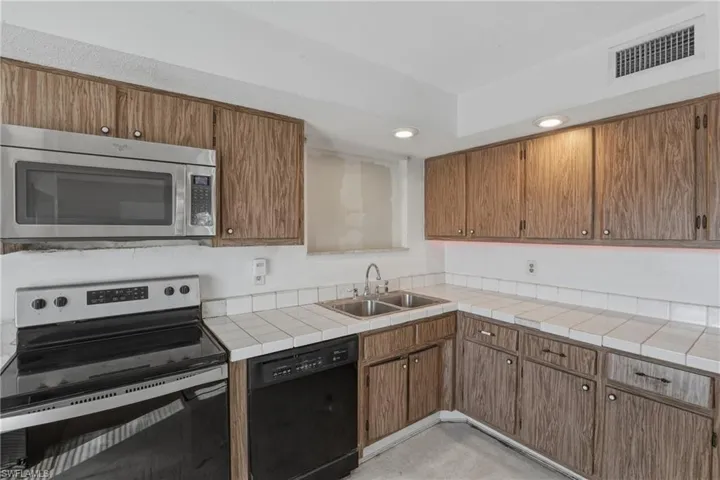 Kitchen with stainless steel appliances, tile counters, wood finish cabinets, and recessed lighting