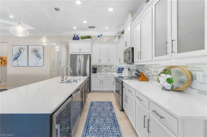 Kitchen with sink, ornamental molding, appliances with stainless steel finishes, tasteful backsplash, and a center island with sink