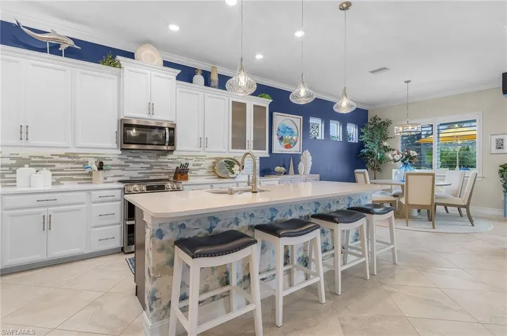 Kitchen featuring decorative backsplash, pendant lighting, a kitchen bar, white cabinetry, and appliances with stainless steel finishes