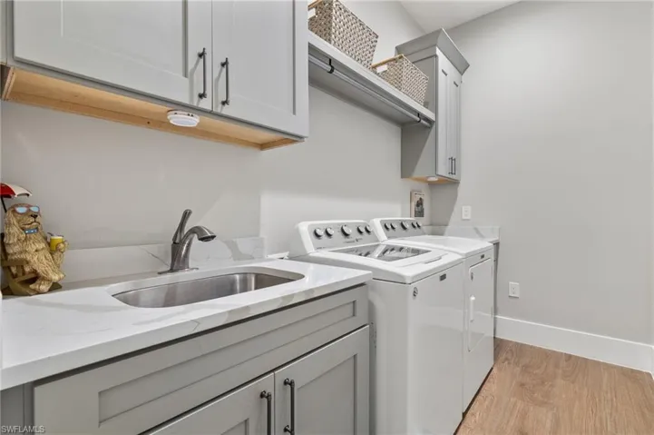 Clothes washing area featuring sink, light hardwood / wood-style floors, independent washer and dryer, and cabinets