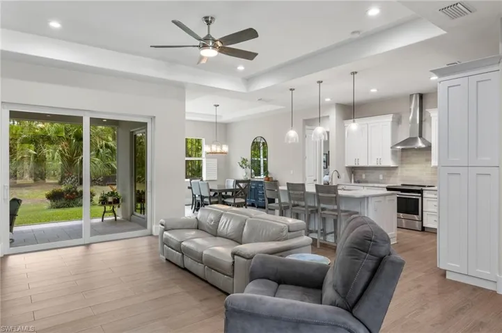 Living room with plenty of natural light, light hardwood / wood-style flooring, a raised ceiling, and ceiling fan with notable chandelier