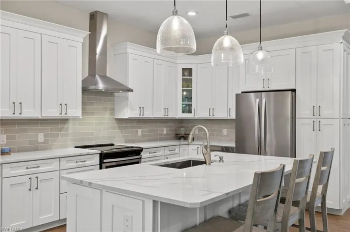 Kitchen featuring stainless steel appliances, hardwood / wood-style floors, wall chimney exhaust hood, decorative light fixtures, and tasteful backsplash