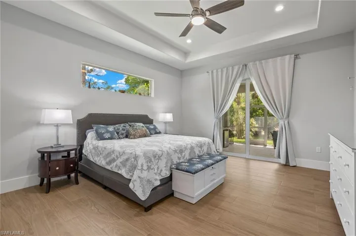 Bedroom with ceiling fan, access to exterior, light hardwood / wood-style floors, and a tray ceiling