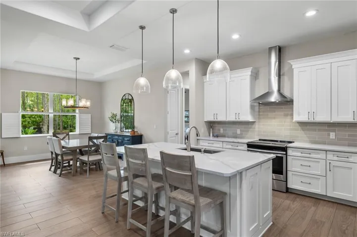 Kitchen featuring stainless steel stove, a raised ceiling, hardwood / wood-style floors, wall chimney exhaust hood, and sink
